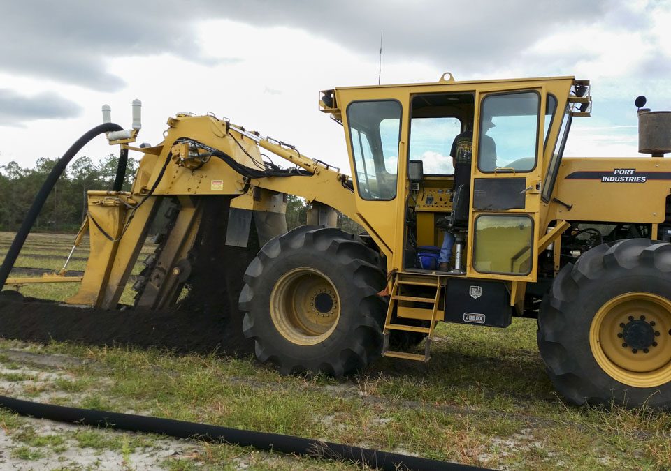 Large trenching tractor installing sub-irrigation drain tiles in a farm