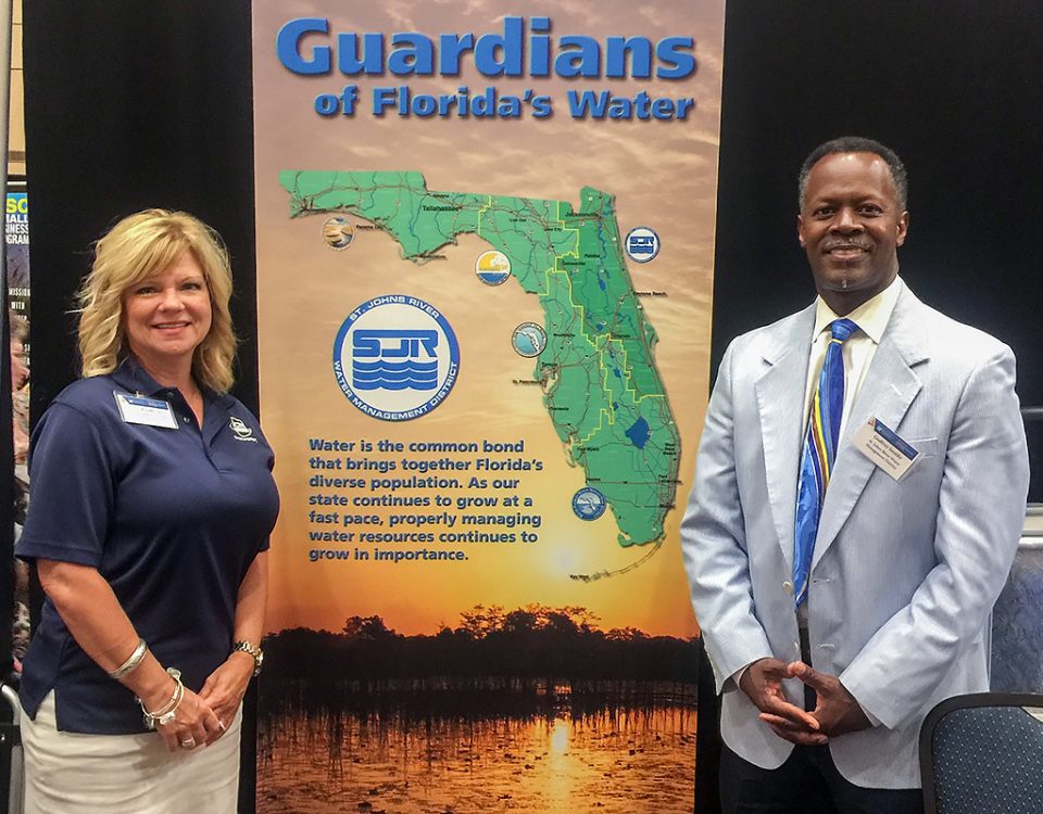 Two procurement staff members standing with district banner stand