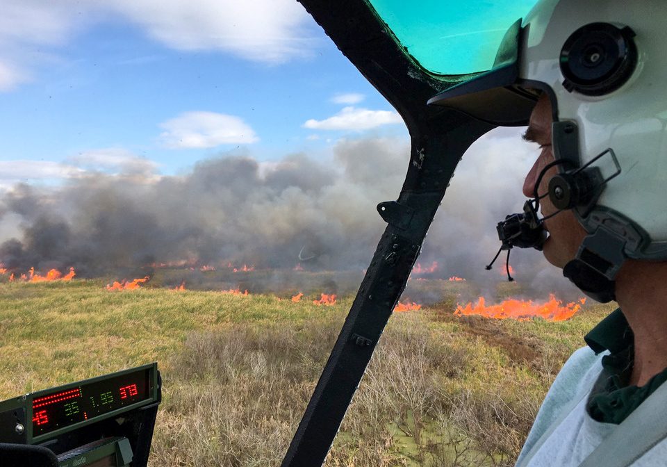 Person in helicopter looking at a fire burning in a marsh