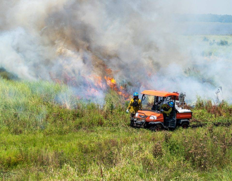 two district employees next to a prescribed fire